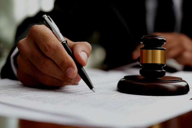 Person signing a document next to a judge’s gavel.